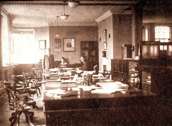 Photograph of office showing a long table surrounded by chairs with only three people around it